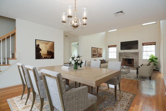 dining space with visible vents, an inviting chandelier, a brick fireplace, light wood-style floors, and stairway