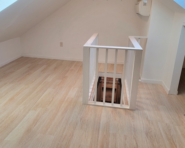 bonus room with a wall mounted air conditioner, light hardwood / wood-style flooring, and vaulted ceiling with skylight