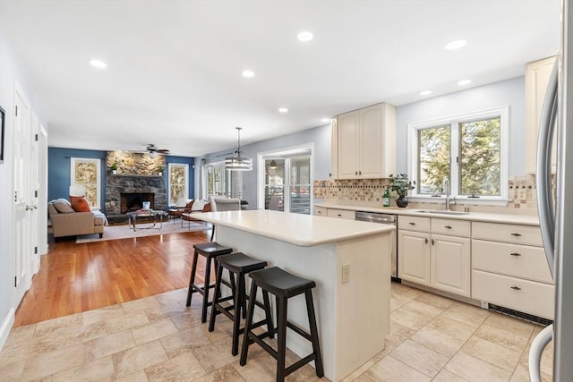 kitchen with a fireplace, sink, backsplash, a kitchen breakfast bar, and hanging light fixtures