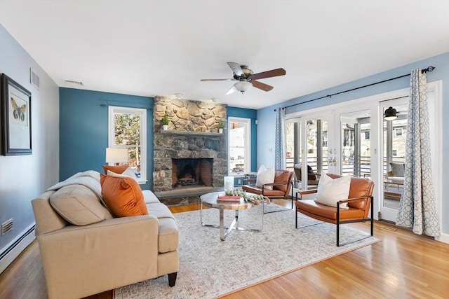 living room with a stone fireplace, a baseboard heating unit, hardwood / wood-style floors, and ceiling fan