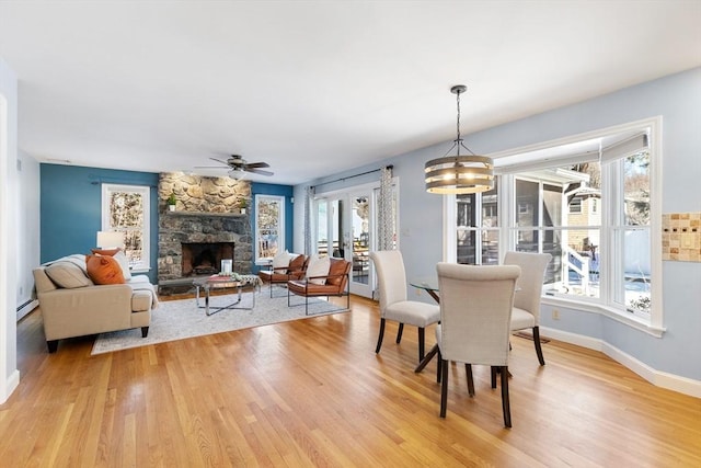 dining room with hardwood / wood-style floors, a stone fireplace, ceiling fan, and a baseboard heating unit