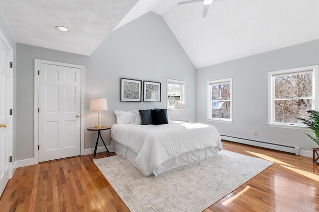 bedroom with ceiling fan, high vaulted ceiling, light hardwood / wood-style floors, and a baseboard heating unit