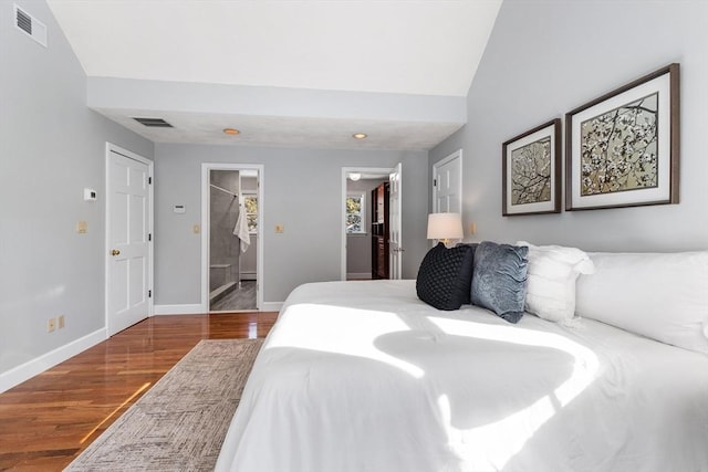 bedroom featuring lofted ceiling, ensuite bath, wood-type flooring, a walk in closet, and a closet