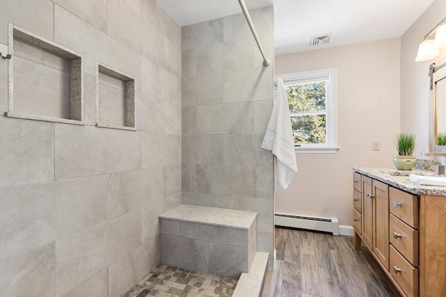 bathroom featuring baseboard heating, tiled shower, vanity, and wood-type flooring