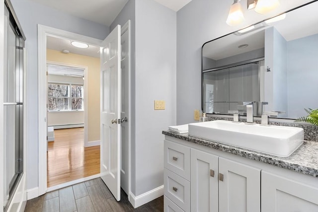 bathroom with vanity, hardwood / wood-style floors, a shower with shower door, and a baseboard heating unit