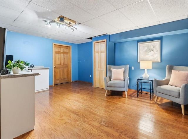 living area with a drop ceiling and light wood-type flooring