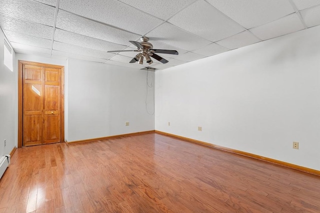 empty room with ceiling fan, a paneled ceiling, baseboard heating, and light wood-type flooring