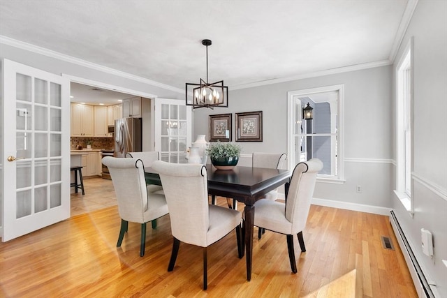 dining space with an inviting chandelier, baseboard heating, crown molding, light wood-type flooring, and french doors