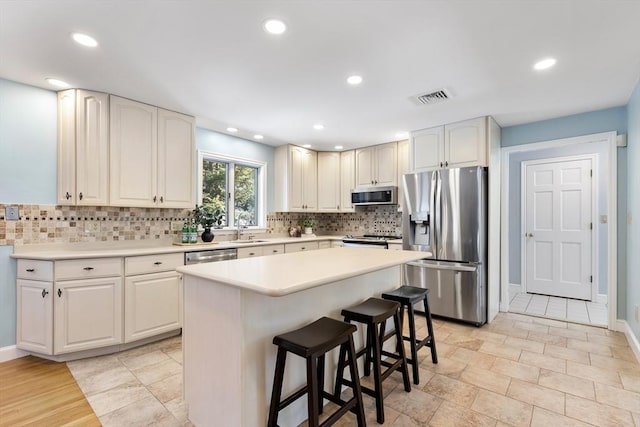 kitchen with sink, appliances with stainless steel finishes, a kitchen island, a kitchen bar, and decorative backsplash