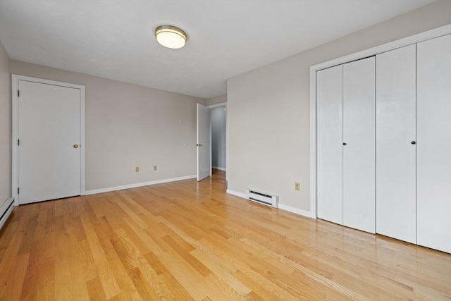 unfurnished bedroom featuring a baseboard heating unit, light wood-style floors, and baseboards