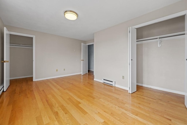 unfurnished bedroom featuring a baseboard radiator, light wood-type flooring, baseboards, and two closets