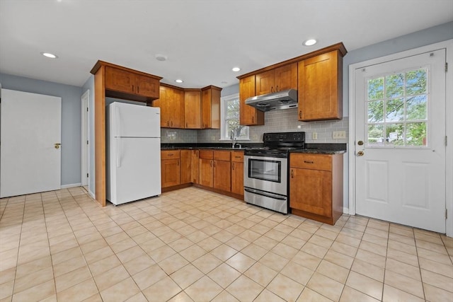 kitchen featuring freestanding refrigerator, stainless steel electric range, under cabinet range hood, dark countertops, and decorative backsplash