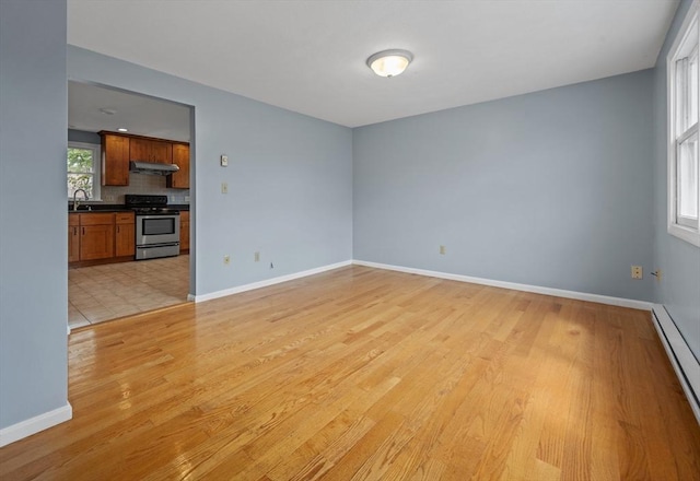 empty room featuring a baseboard radiator, a sink, light wood finished floors, and baseboards