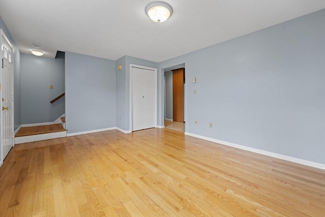 spare room with baseboards, light wood-type flooring, and stairway