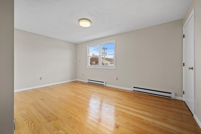 spare room featuring a baseboard heating unit, light wood-style floors, and baseboards