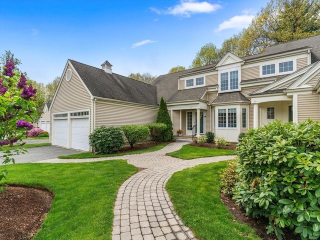 view of front facade with a front lawn, driveway, a shingled roof, a chimney, and an attached garage