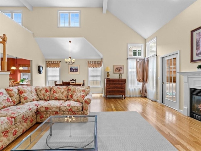 living room featuring high vaulted ceiling, beamed ceiling, wood finished floors, a chandelier, and a glass covered fireplace