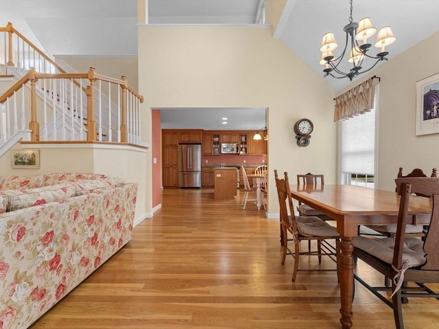 dining area with light wood-style flooring, high vaulted ceiling, stairs, and a chandelier