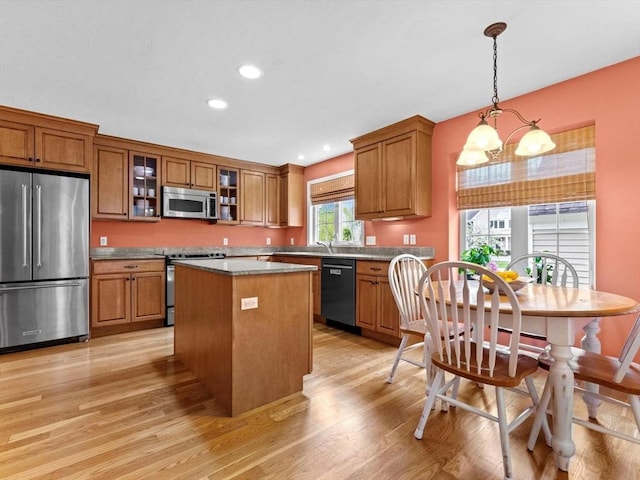 kitchen featuring appliances with stainless steel finishes, brown cabinetry, light wood-type flooring, a center island, and glass insert cabinets