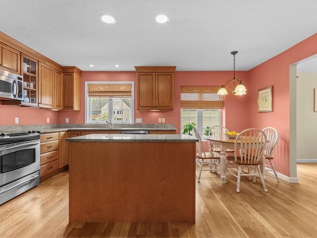 kitchen featuring appliances with stainless steel finishes, a kitchen island, brown cabinets, glass insert cabinets, and light wood-style flooring
