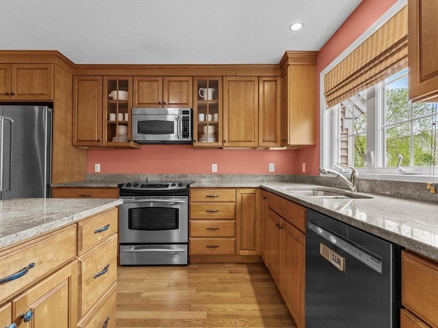 kitchen featuring stainless steel appliances, a sink, light wood-style flooring, brown cabinetry, and light stone countertops