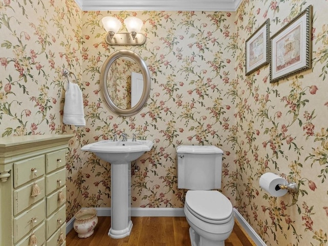 half bath featuring wood finished floors, crown molding, toilet, wallpapered walls, and baseboards