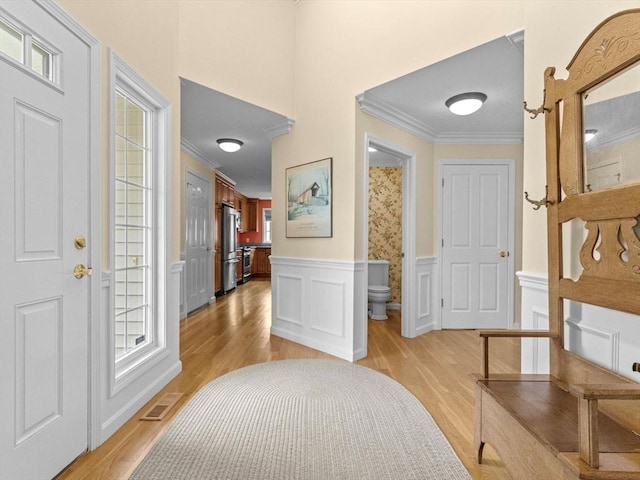 foyer entrance with light wood-type flooring, ornamental molding, healthy amount of natural light, wainscoting, and a decorative wall