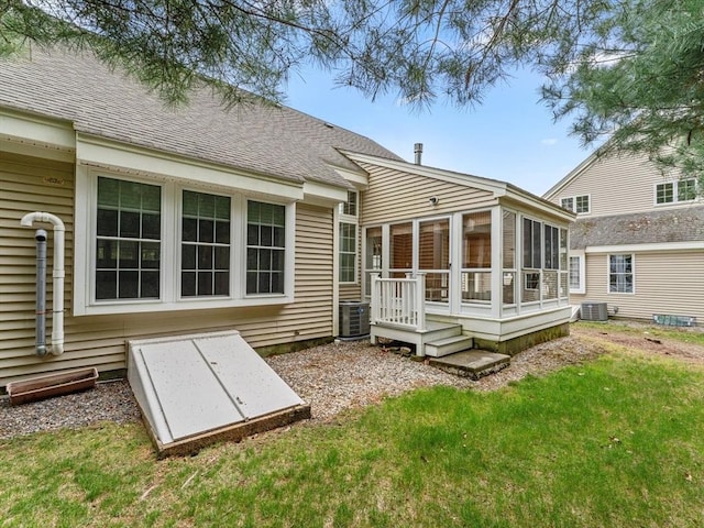 back of property with a sunroom, cooling unit, a lawn, and a shingled roof