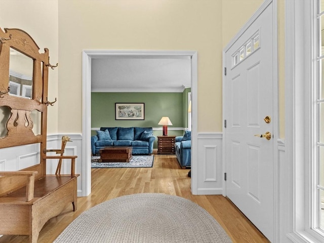 foyer entrance with light wood finished floors, ornamental molding, and wainscoting