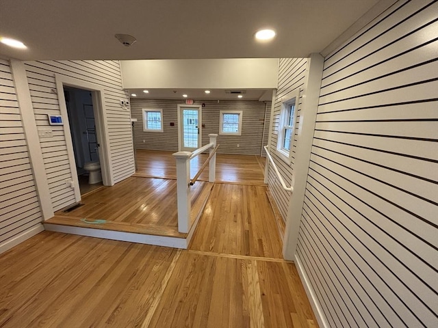 interior space with light wood-style floors, recessed lighting, wood walls, and an upstairs landing