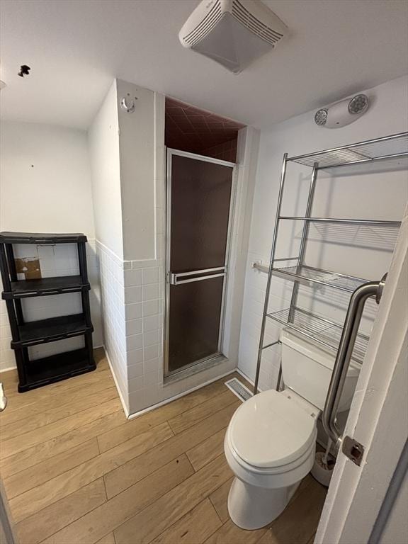 full bathroom featuring toilet, wood finished floors, visible vents, tile walls, and a stall shower