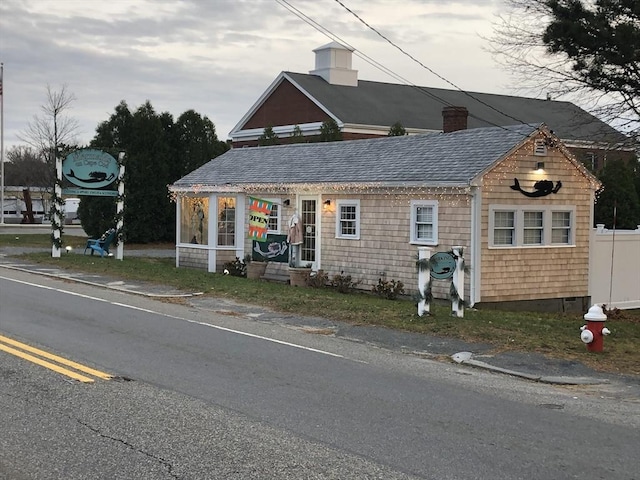 view of front facade with a chimney, fence, and roof with shingles