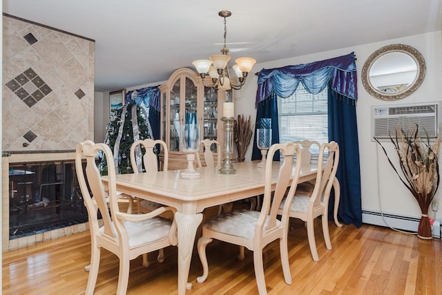 dining space with wood-type flooring, a wall mounted air conditioner, baseboard heating, a tile fireplace, and a notable chandelier