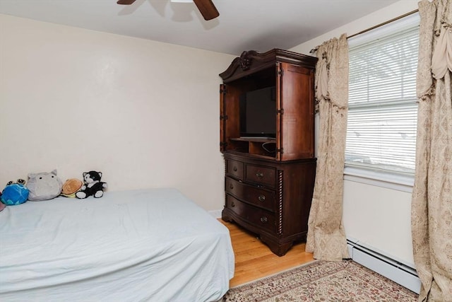 bedroom featuring ceiling fan, a baseboard heating unit, and light wood-type flooring