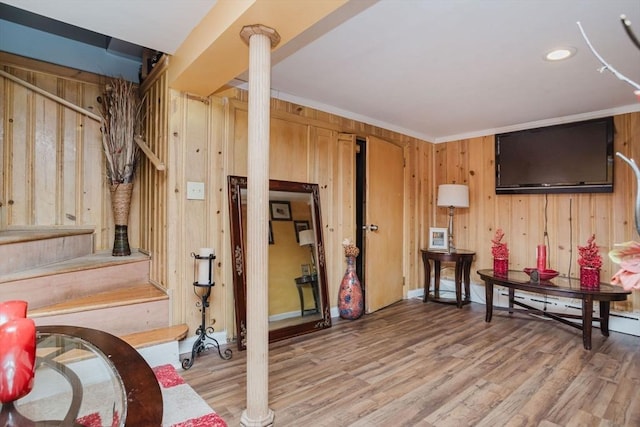 interior space with crown molding, wooden walls, decorative columns, and light hardwood / wood-style flooring