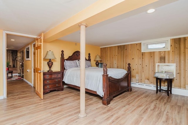 bedroom featuring a baseboard radiator, wooden walls, and light hardwood / wood-style flooring