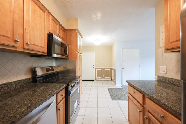 3 Dailey St Unit I, Attleboro, MA 02703 - kitchen featuring appliances with stainless steel finishes, a wainscoted wall, decorative backsplash, dark stone countertops, and light tile patterned floors