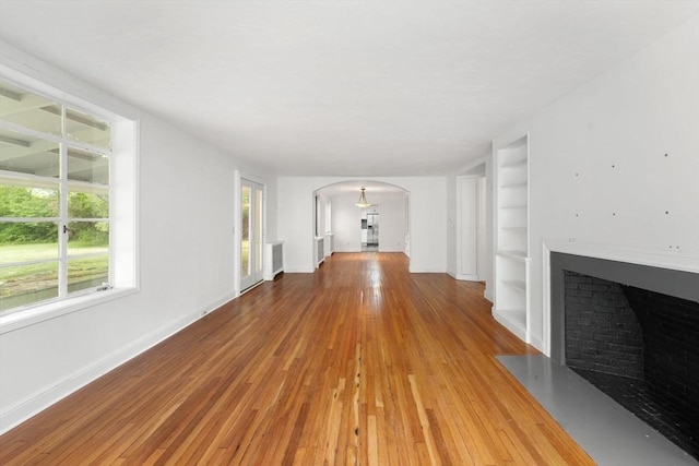 220 Prospect St, Seekonk, MA 02771 - unfurnished living room featuring arched walkways, built in shelves, light wood-style floors, a fireplace with flush hearth, and baseboards