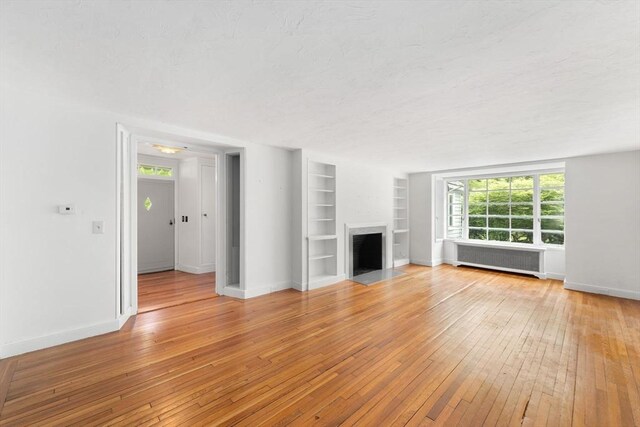 220 Prospect St, Seekonk, MA 02771 - unfurnished living room featuring radiator, light wood finished floors, built in shelves, a fireplace with flush hearth, and baseboards