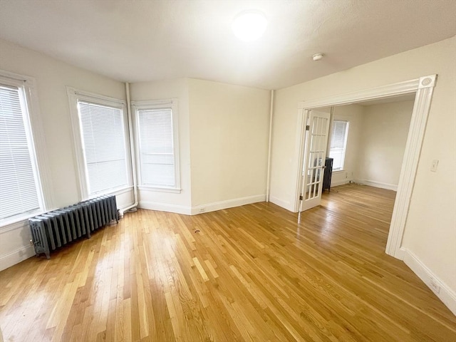 unfurnished room with radiator, baseboards, and light wood-style floors