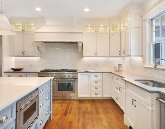 kitchen with premium range hood, sink, light wood-type flooring, high end stove, and white cabinetry