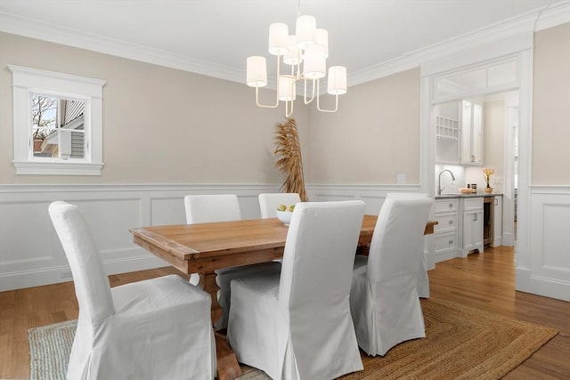 dining space with a chandelier, light wood-type flooring, wine cooler, and crown molding