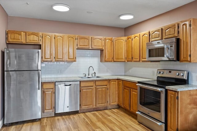 kitchen with tasteful backsplash, light wood-type flooring, light countertops, stainless steel appliances, and a sink