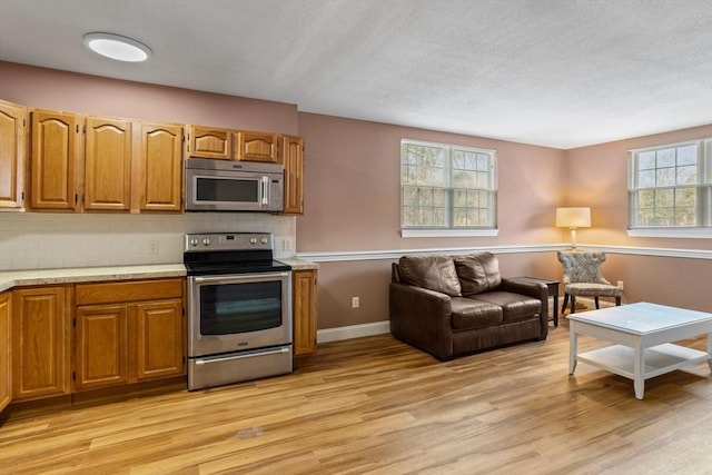 kitchen featuring light wood-style flooring, tasteful backsplash, open floor plan, appliances with stainless steel finishes, and light countertops