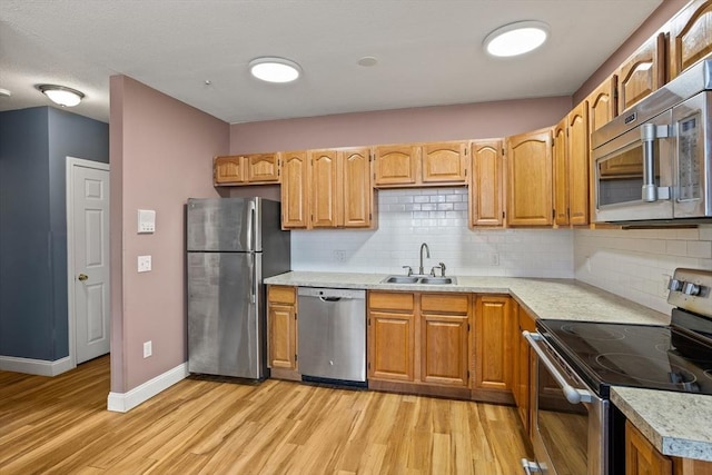 kitchen with light wood-type flooring, a sink, backsplash, appliances with stainless steel finishes, and light countertops