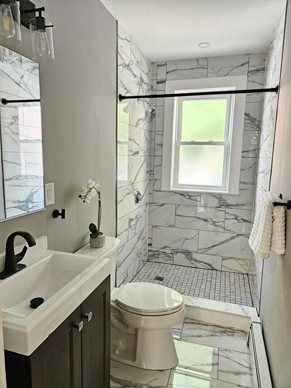 bathroom featuring baseboard heating, tiled shower, vanity, and toilet