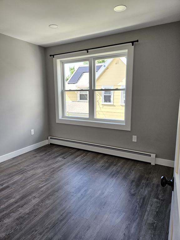 unfurnished room with a baseboard heating unit and dark hardwood / wood-style flooring