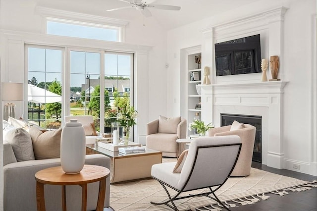 living area with baseboards, light wood-type flooring, a high end fireplace, and a ceiling fan