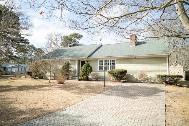 view of front of property with a shingled roof, an outdoor structure, a storage unit, and a chimney