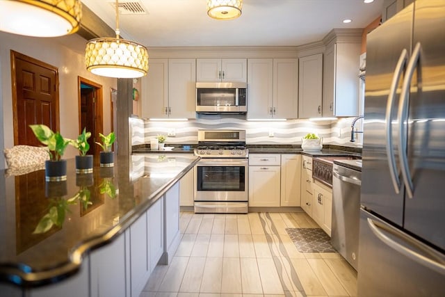 kitchen with visible vents, dark stone counters, appliances with stainless steel finishes, decorative backsplash, and hanging light fixtures